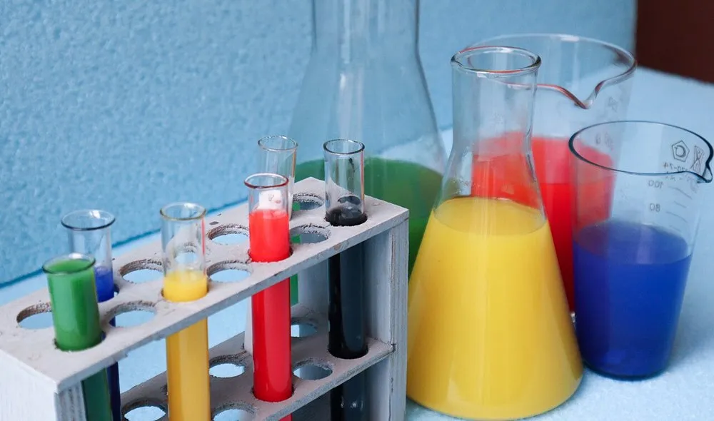 Tubos de ensayo en su gradilla, un matraz Erlenmeyer y un vaso de precipitados con disoluciones de colores