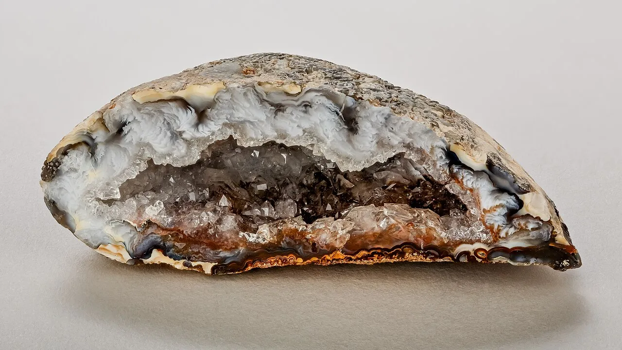 Una geoda partida por la mitad: por fuera parece un pedrusco cualquiera, y por dentro el hueco está tapizado de cristales que han crecido hacia el centro.