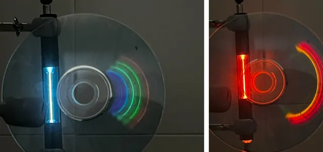Un tubo de mercurio, a la izquierda, y uno de neón, mirados a través de un CD, que separa la luz en colores. El mercurio da sobre todo azul y verde; el neón, rojo y naranja